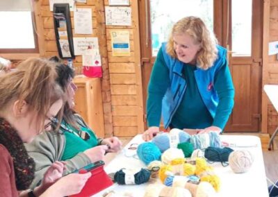 Volunteer Center Officer chatting to ladies knitting. Lots of balls of wool on the table.