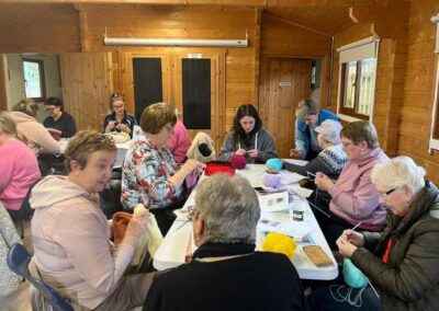 Group of ladies knitting and chatting. Volunteer organiser in background supporting