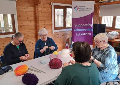 Group of ladies knitting and chatting with volunteer pull up Supporting Volunteering in Leitrim in the background