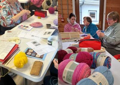 Table with knitting patterns scattered. Older lady teaching younger lady to knit